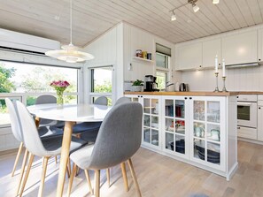 Eine moderne Küche mit weißen Schränken, einer zentralen Kochinsel mit Spüle und einem Essbereich mit rundem Tisch und Stühlen.
