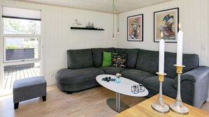 Ein modernes Wohnzimmer mit einem grauen Ecksofa, einem kleinen weißen Couchtisch und zwei weißen Kerzen auf einem Holztisch.