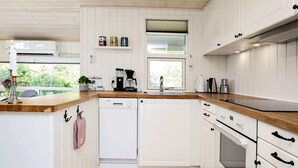 Eine moderne Küche mit weißen Schränken, einer Holz Arbeitsplatte, einem Geschirrspüler von Bosch, einer Kaffeemaschine und einem Fenster für natürliches Licht.