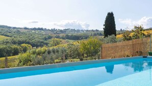 Une piscine d’eau cristalline, d’un bleu éclatant, avec vue sur un vignoble et des collines verdoyantes à l’arrière-plan.