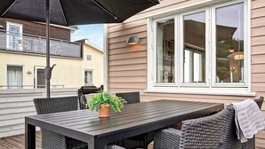 Une terrasse avec une table et des chaises, un pot de fleurs et un grand parasol.