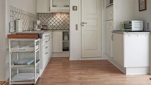 Une cuisine compacte avec des meubles blancs, un four à micro-ondes, une machine à café et un pare-feu en carreaux.