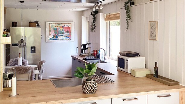 A modern kitchen with wooden countertops, a built-in stove, and a sink. There is a dining area with a table and chairs, and a small island with a plant. - 12 Person Holiday Home in Vaeggerlose (Vaeggerlose)