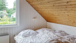 A bedroom with a sloped wooden ceiling, a window with a view of greenery and houses, and a white bed with pillows. - 12 Person Holiday Home in Vaeggerlose (Vaeggerlose)
