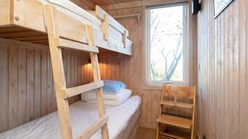 A wooden cabin room with bunk beds, a chair, and a window.