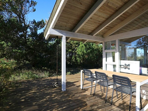 An outdoor wooden deck with a table and chairs, surrounded by trees.