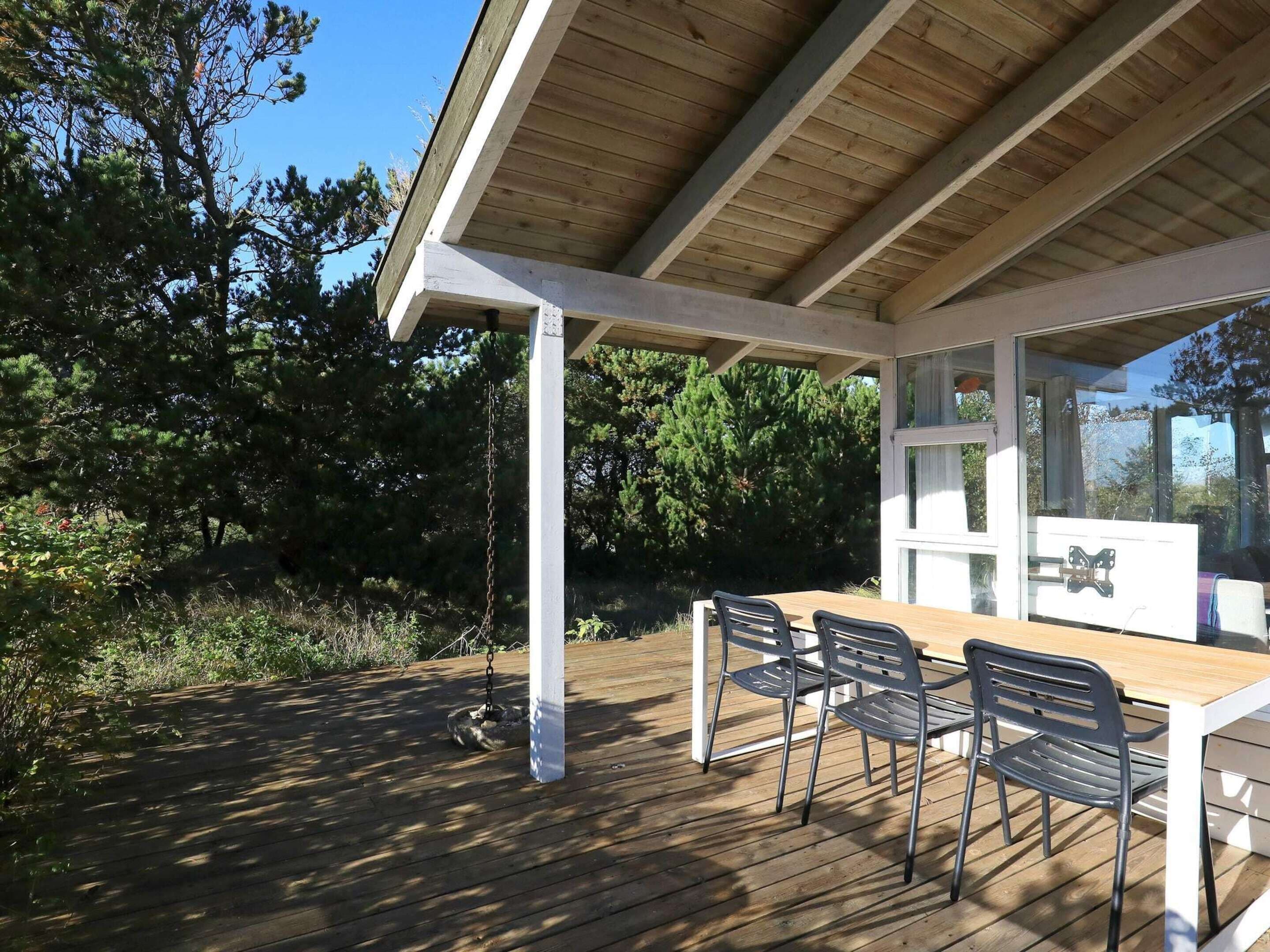 Un espacio al aire libre techado con piso de madera, una mesa y cuatro sillas.