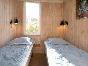 Une chambre avec deux lits simples, une fenêtre et deux lampes fixées au mur.