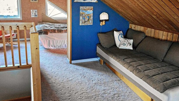 Un dormitorio acogedor en el ático con una pared azul de acento, techo inclinado de madera, una cama litera y un sofá.