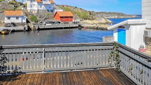 Terraza de madera con barandilla que da a un puerto con barcos y casas.