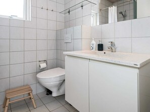 Une salle de bain moderne comprenant des toilettes, un petit tabouret en bois, un lavabo avec un miroir et un espace douche.