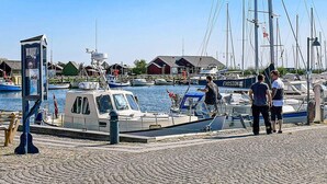 En småbåtshamn med förtöjda båtar, en liten båt med en hytt och en byggnad med ett rött tak i bakgrunden.