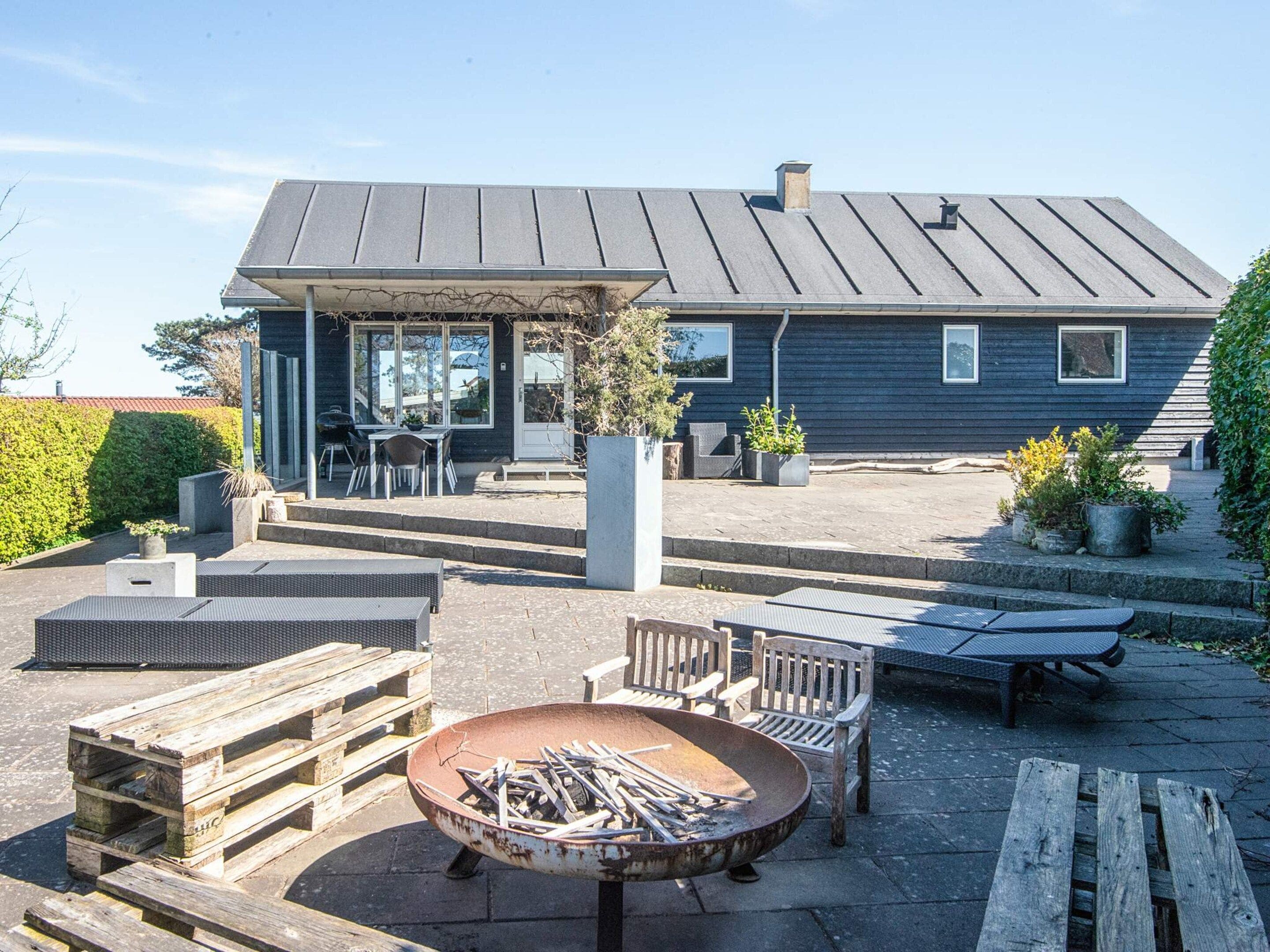 A modern house with a patio area featuring outdoor furniture, a fire pit, and a well-maintained garden.