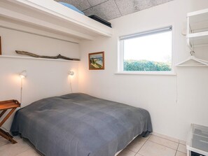 A bedroom with a bed, a window, a wall-mounted shelf, a picture, and a hanging rack.