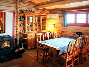 Un interior de cabaña acogedor, con una mesa de comedor de madera, sillas, una chimenea y un aparador con puertas de vidrio.