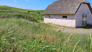 A thatched-roof house with a small window and a door, surrounded by grassy fields. - 16 Person Holiday Home in Ulfborg (Ulfborg)