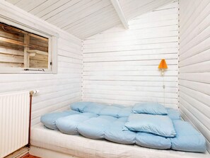 A small, white-paneled room with a bed, a window, and a wall-mounted lamp.