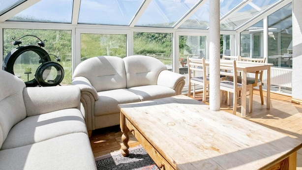 A conservatory with a sofa, table, and chairs, large windows, and a clock. - 16 Person Holiday Home in Ulfborg (Ulfborg)