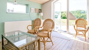 A room with a glass-top table, wicker chairs, a white radiator, and a view through a glass door to an outdoor area. - 16 Person Holiday Home in Ulfborg (Ulfborg)
