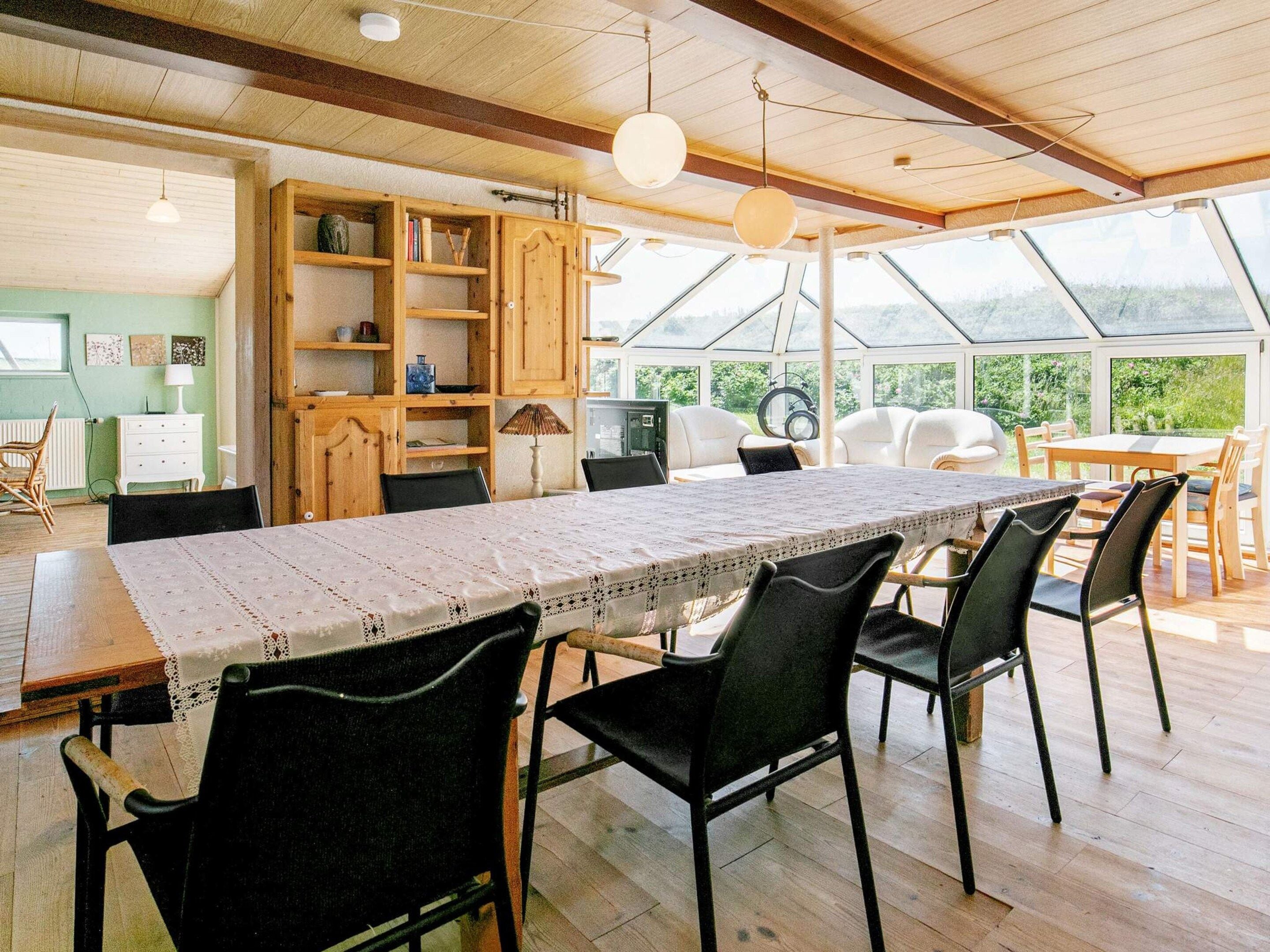 Un comedor amplio con una mesa larga y sillas, un mueble de madera con estantes, y vistas a través de un ventanal.