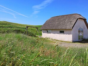 A thatched-roof house with a small porch, surrounded by grassy fields.
