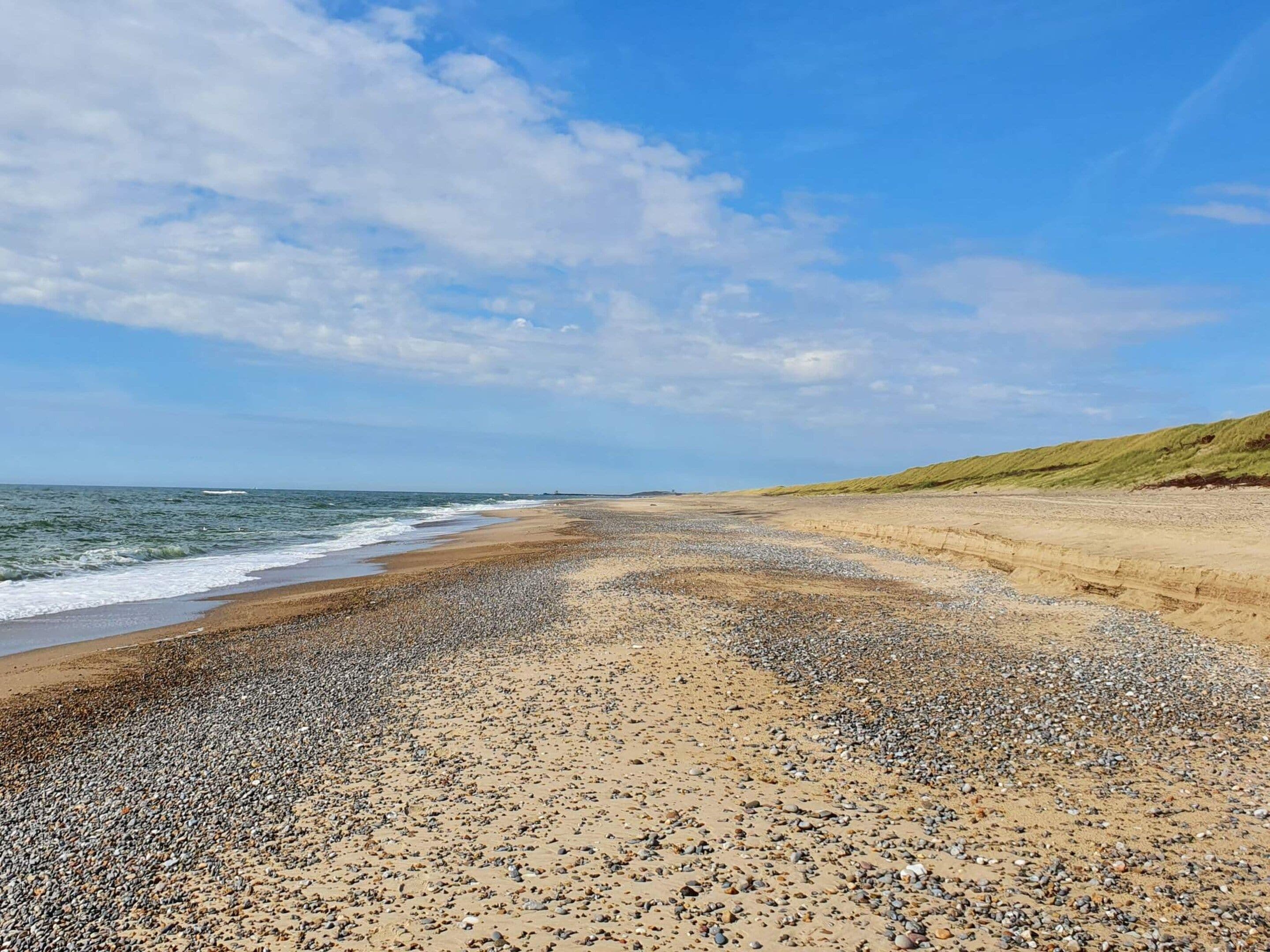 Uma praia com pedras e areia, céu claro e ondas suaves.
