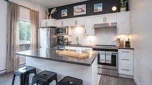 A modern kitchen with white cabinets, stainless steel appliances, and a central island. - Cozy and Modern Getaway (Revelstoke)
