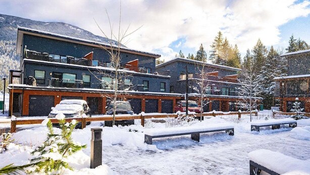 A modern building with a wooden deck and a snow-covered parking area. - Cozy and Modern Getaway (Revelstoke)