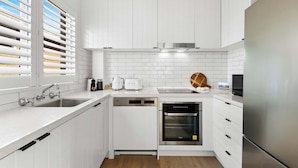 A modern kitchen with white cabinetry, a stainless steel refrigerator, a built-in oven, and a dishwasher. - Coogee by the Coast  (Coogee)