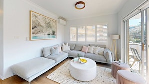 A modern living room with a sectional sofa, a round coffee table, and a large window with blinds. - Coogee by the Coast  (Coogee)