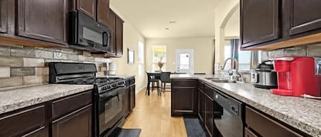 A modern kitchen with dark wood cabinets, a stainless steel range, and a red coffee maker.