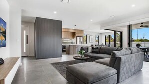 A modern living room with a grey sectional sofa, a coffee table, and a kitchen in the background.