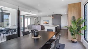 A modern kitchen with a central island, a dining area with a long table, and a large window with a view of the outdoors.