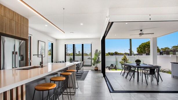 A modern kitchen with a long counter, bar stools, and a dining area with a table and chairs.