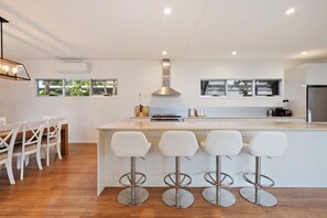 Une cuisine moderne dotée d’un îlot central, de tabourets de bar et d’un coin repas avec une table et des chaises en bois.