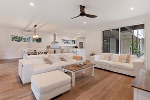 A modern living room with white sofas, a wooden coffee table, and a ceiling fan.