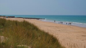 Een strand met mensen die langs de kust wandelen, een heldere lucht en een rustige zee.