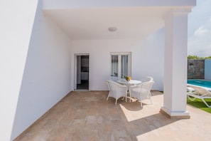 Um quarto branco com piso de azulejos, uma mesa com cadeiras, uma janela e vista para uma piscina.