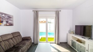 Een moderne woonkamer met een bank, een salontafel, een televisie en een schuifdeur naar een zwembad.