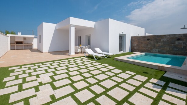 Een modern huis met een zwembad, een terras met lounge fauteuils en een keurig onderhouden gazon.