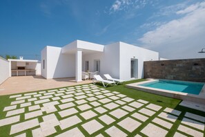 Uma casa moderna com piscina, um alpendre com cadeiras de descanso e um gramado bem cuidado.
