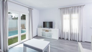Een moderne woonkamer met een flatscreen televisie, een witte tafel en een glazen schuifdeur naar een zwembad.