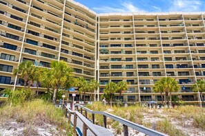 Ein mehrstöckiges Hotel mit Balkonen, einem Sandstrand und einer Holzterrasse.