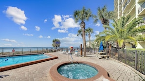 A pool area with a hot tub, lounge chairs, and palm trees.