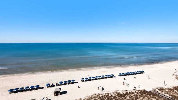 A beach with rows of blue umbrellas and beach chairs, a lifeguard tower, and a clear view of the ocean.