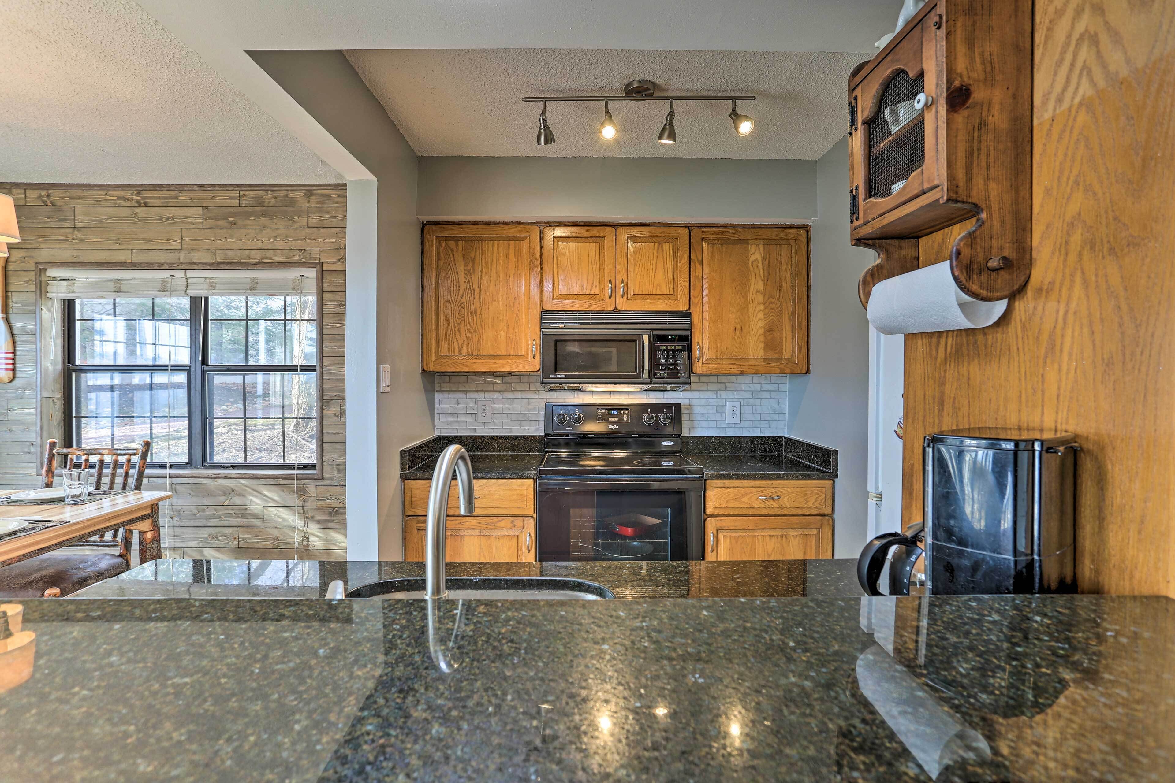 A kitchen with wooden cabinets, a stainless steel microwave, a stove, and a sink.