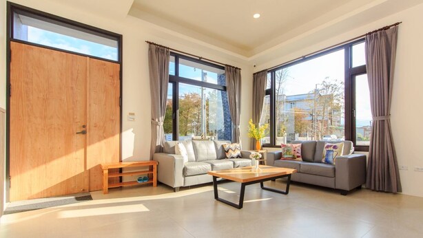A spacious living room with a sofa set, a coffee table, and large windows offering a view of the outside. - Classic Villa B&B (Dongshan)
