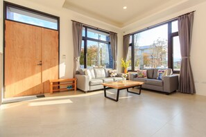 A spacious living room with a sofa set, a coffee table, and large windows offering a view of the outside. - Classic Villa B&B (Dongshan)