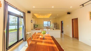 A spacious dining area with a long wooden table, a kitchen in the background, and large windows offering a view of the outdoors. - Classic Villa B&B (Dongshan)