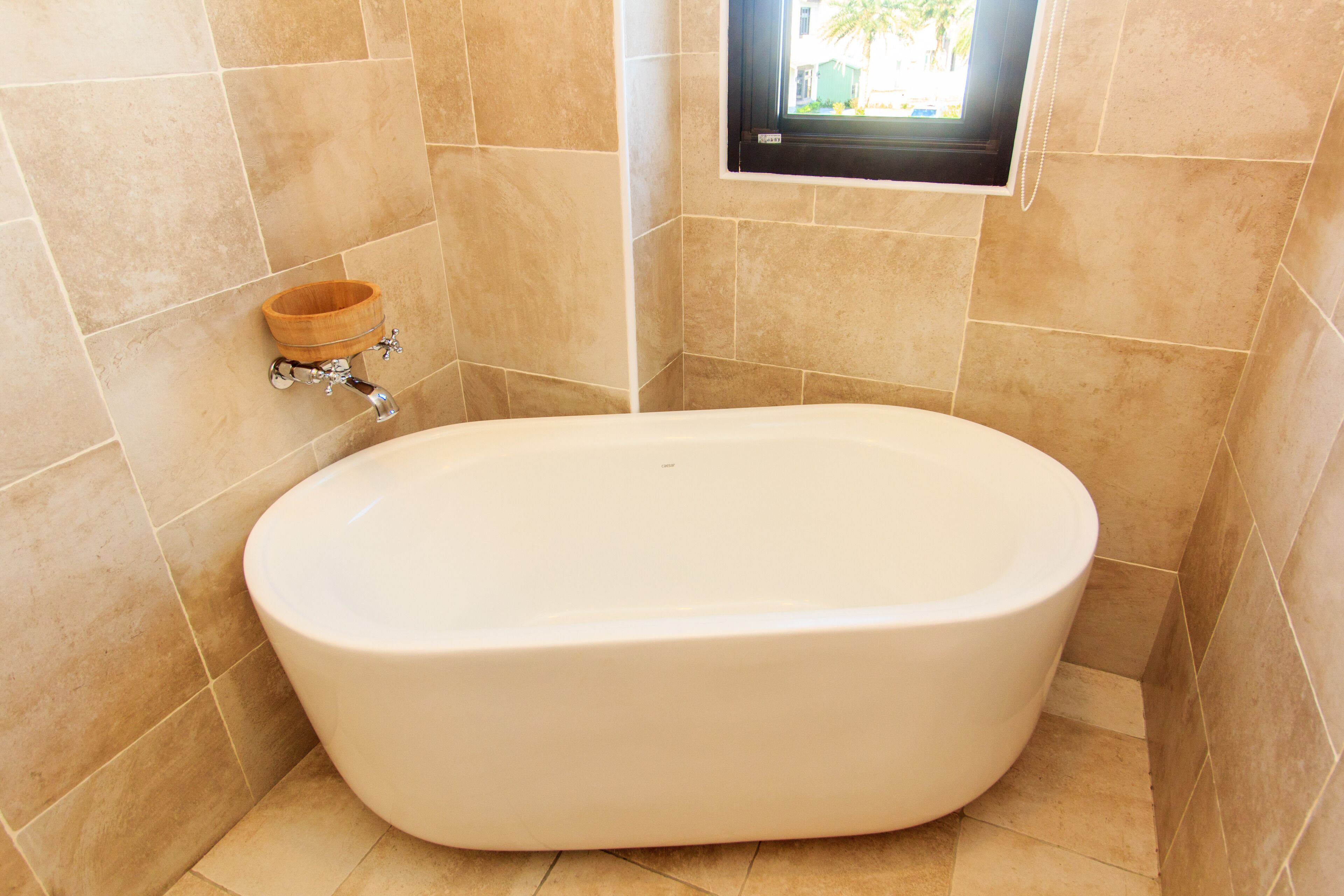 A modern bathroom with a freestanding bathtub, a wooden bath tray, and a small window.